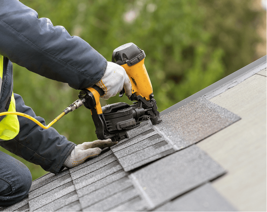 Worker using nail gun on roof shingles.