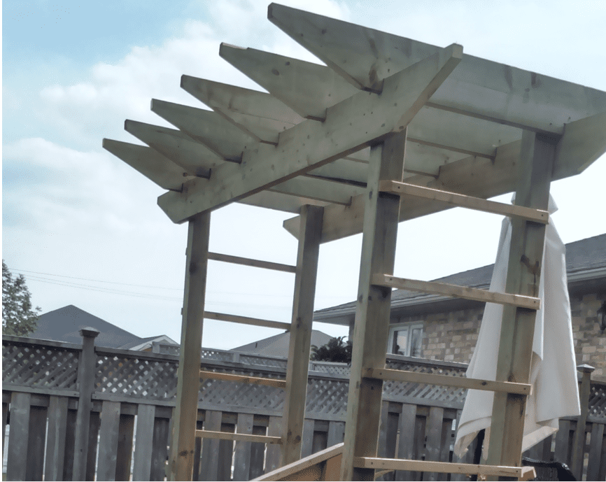 Wooden pergola under partly cloudy sky.